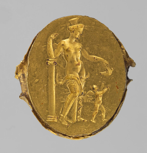 Golden finger ring with a elief of Aphrodite and Eros. The goddess is wearing a polos crown, her right arm resting on a column. With her left hand she is giving a dove to her son Eros who quickly makes a grab for the flying bird that is about to fly off.