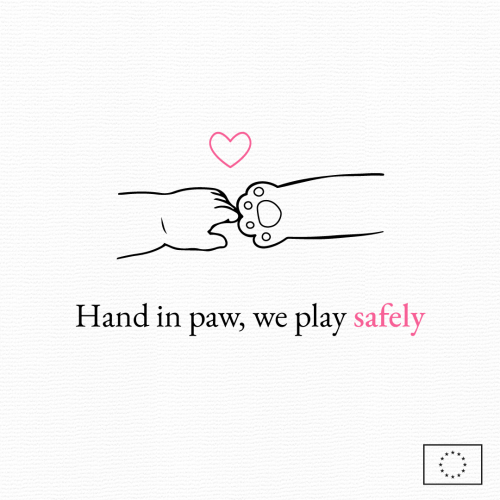 A child's hand touching the paw of a teddy bear with a pink heart on top.
