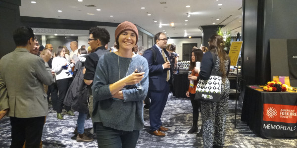 Photo of me in a crowd at the hotel. I'm smiling, holding a glass of red, and wearing a blue sweater and a red knit hat
