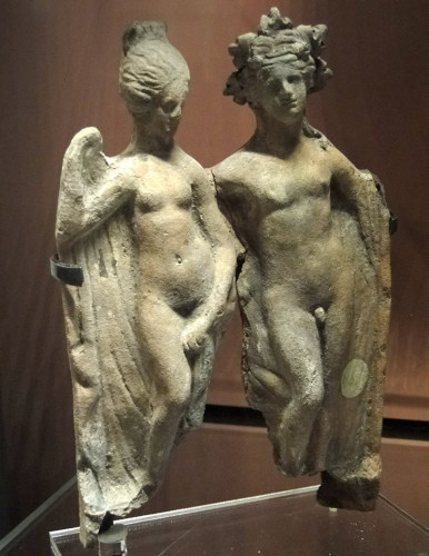 Terracotta figures of Dionysos and Ariadne. They used to be coloured but only very few traces remain. Both are depicted in the nude with Ariadne holding a large himation behind her back and Dionysos leaning against a tree stump, possible part of Ariadne's large himation behind his hips but parts of it are missing. He is crowned with vine or ivy. Both have about the same height.
