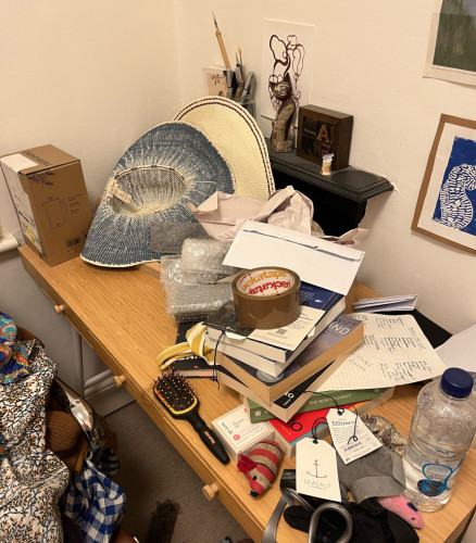 A writer's desk strewn with all the clutter of the creative life: books, notes, pens, hats… and is that a hairbrush?