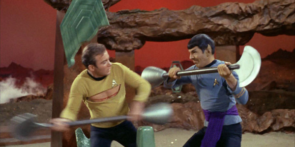 Kirk and Spock battling with weapons. Kirk is injured with a gash across his chest 