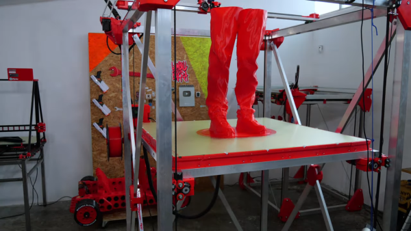 A massive 3D printer in action, showing just the legs of a figure as they are printed