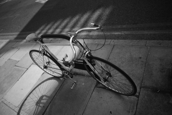 Black and white photo of a bicycle locked to a stand on a pavement in London