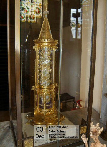 A golden reliquary in the shape of a small tower. Through glass one can see the wrapped remains inside.