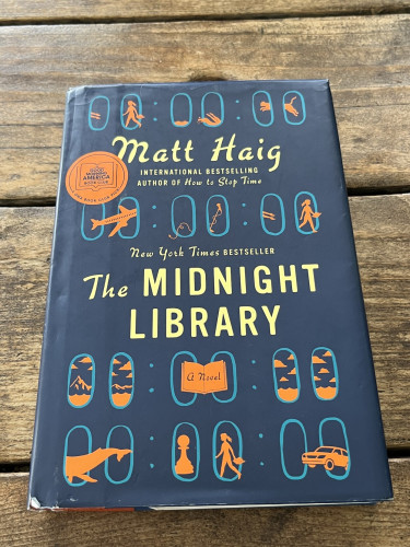 A used hardcover copy of The Midnight Library by Matt Haig on a wooden table.