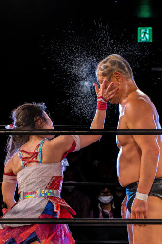 Mei Suruga slapping Minoru Suzuki, cinematically splattering the sweat off of him against a stark black background.