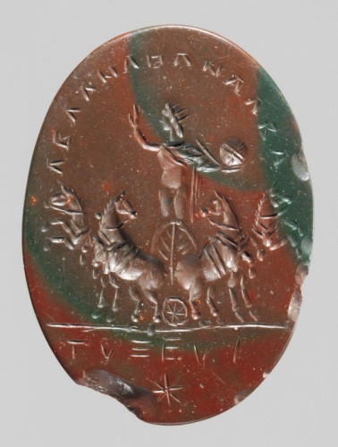 Engraved gem of red and green jasper depicting Helios standing upright in his chariot drawn by four prancing horses. He wears a cloak wrapped around his shoulders that is closed over his right arm. He wears a crown of which we see three spikes as his head is turned towards the right. His right hand is raised and he holds a globe in his left. A Greek inscription is curved above him and below the hooves of the horses. A stylised star decorates the bottom.