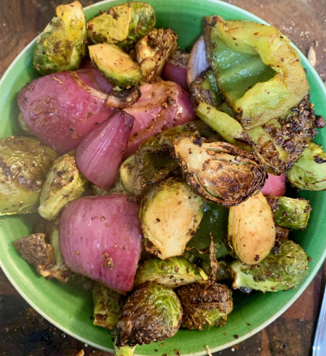 A  bowl full of halved brussels sprouts, red onion cut into eighths, and chunks of green bell pepper, roasted until edges are brown.