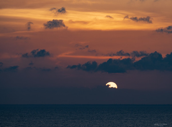 Part of the sun is visible through the clouds over the sea. 