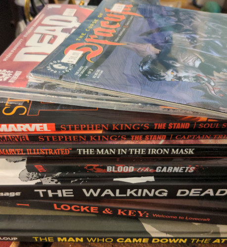 a pile of graphic novels including Stephen King's The Stand, Locke & Key, The Walking Dead, The Man in the Iron Mask, The Man Who Came Down from the Attic and issues of The Curse of Dracula and Dead Day