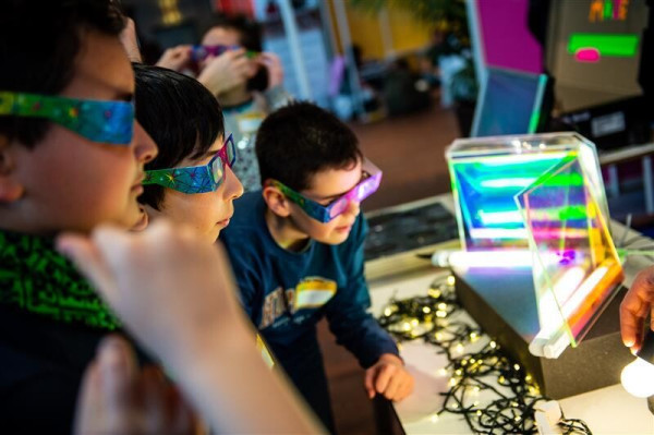 Children wearing coloured glasses looking at a science experiment with lights and colours. 