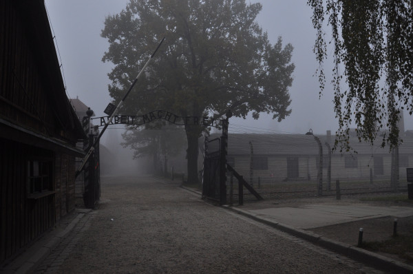 The Arbeit macht frei gate to the former Auschwitz I camp. The barbed wire fences and kitchen building on the right are visible. A foggy day.