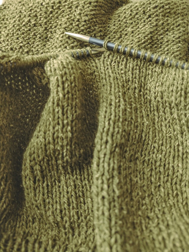 Close up of a knitting project. The yarn is moss green and has some structure to it. The knitting is plain stockinette.