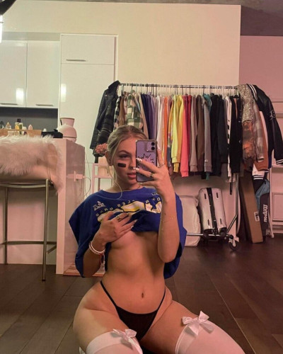 Me taking a mirror selfie while i have my LA rams shirt pulled up not wearing a bra im cupping my right titty in my hand and holding my phone in the other im wearing a black thong that captures the curves of my hips i have white knee high socks on with white bows on top