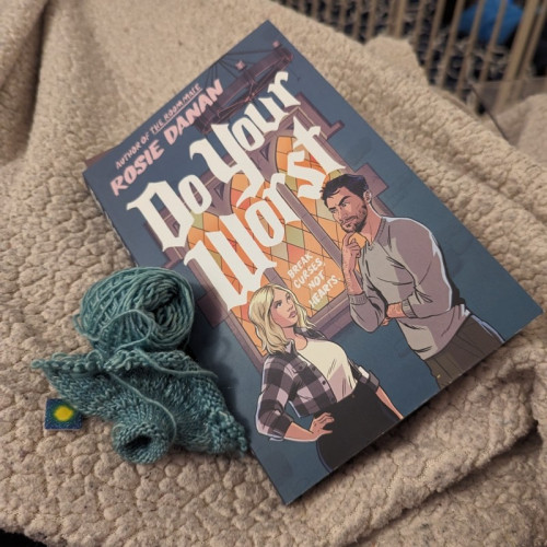 A partially unravelled knit bauble sits next to a copy of Do Your Worst.
