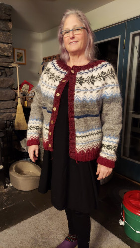 White woman wearing glasses and with shoulder length gray hair is wearing a stranded colorwork knit cardigan.