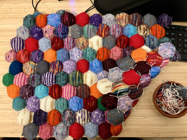 A bunch of knitted hexagonal shapes, sewed together. One side is flipped over, so you can see the threads on the underside.
