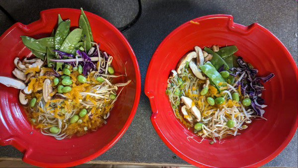 2 red bowls filled with: ramen noodles, broth, red cabbage, bean sprouts, snow peas, edamame, shitaki mushrooms 