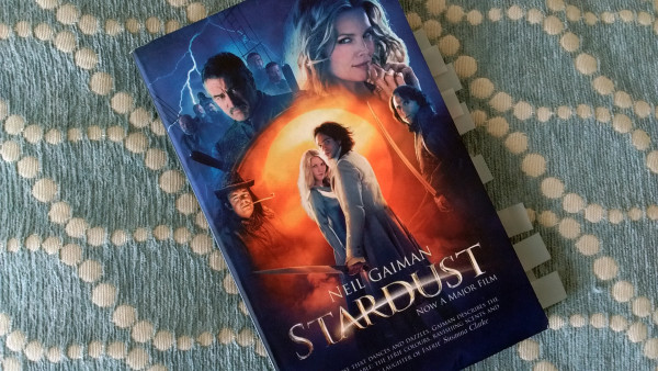 The cover of Stardust by Neil Gaiman shows at its center a couple, she's blonde and looks directly at us, he has long hair and wear a long coat, while surrounded by the faces of those who wish to keep them apart: A beautiful witch, the Capital of a flying pirate boat, seven ghost brothers and a few more.