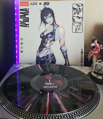 A  Black with Pink, Purple & Red Splatter vinyl record sits on a turntable. Behind the turntable, a vinyl album outer sleeve is displayed. The front cover shows a woman with horns wearing a symbiotic type outfit. 

To the right of the album cover is an anime figure of Yuki Morikawa singing in to a microphone and holding her arm out.