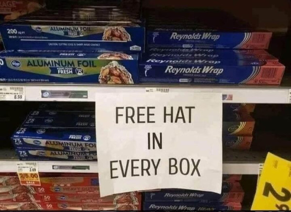 A shelf holding many packets of aluminium foil. A sign taped to the shelf reads, "Free hat in every box."