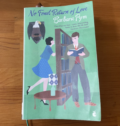 The front cover of the novel No Fond Return of Love by Barbara Pym. It shows an illustration of a brunette woman in blue dress and black heels looking through a tall bookcase at a studious man reading a book. The cover quote is:
‘One of her very best – comic, heartrending, brave; in short, like life itself’
Shirley Hazzard