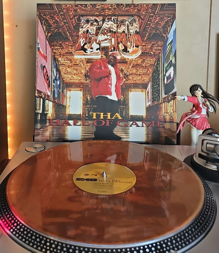 A Red Galaxy vinyl record sits on a turntable. Behind the turntable, a vinyl album outer sleeve is displayed. The front cover shows E-40 posing in a CGI room. 

To the right of the album cover is an anime figure of Yuki Morikawa singing in to a microphone and holding her arm out. 