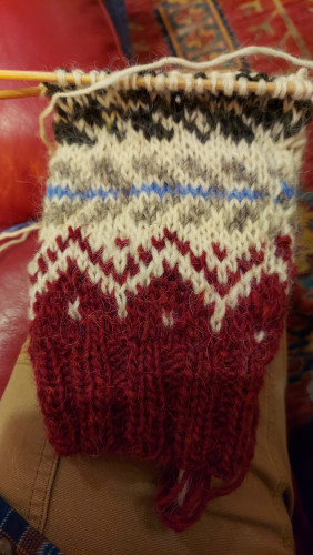 The start of a sleeve for a stranded colorwork knit cardigan. Cuff color: burgundy, design background: white, decorative elements in burgundy, light blue, and forest green. 