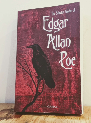 A copy of the book "The Selected Works of Edgar Allan Poe". The cover is a blood red, featuring a single corvid perched on a branch.