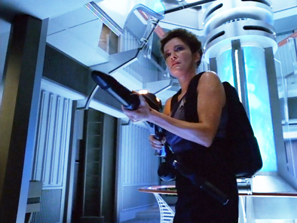 Janeway in a tank top holding a large weapon and glistening in sweat