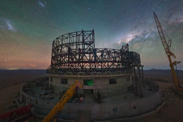 This image, taken in late June 2023, shows a webcam image of the construction site of ESO’s Extremely Large Telescope at Cerro Armazones, in Chile's Atacama Desert. There, engineers and construction workers are currently assembling the structure of the telescope dome at a staggering pace. Visibly changing each day, the steel structure will soon acquire the familiar round shape typical of telescope domes.

The starry background is dominated by the core of the Milky Way, our home galaxy, and the Large and Small Magellanic clouds, two dwarf galaxies that orbit our own.