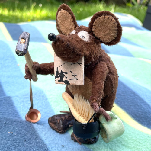 Photo of Minimus the Latin mouse holding multiple tools in both paws and his mouth