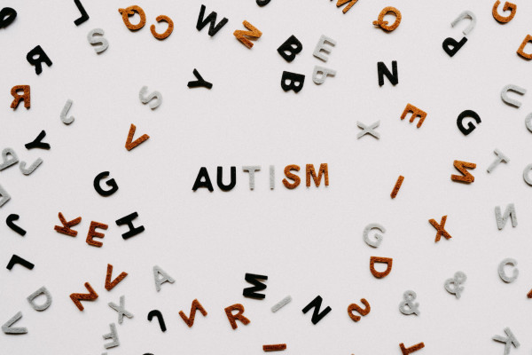 Black, white, and brown letters of the alphabet spread out on a white surface, with the word "autism" in the middle.