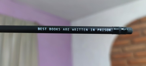 Photo of a black pencil with the legend "BEST BOOKS ARE WRITTEN IN PRISON." written in it. 