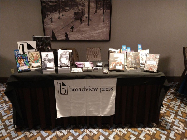 Books are displayed standing up on a table, which is draped in a black table cloth. On the front of the table is a sign that says broadview press.