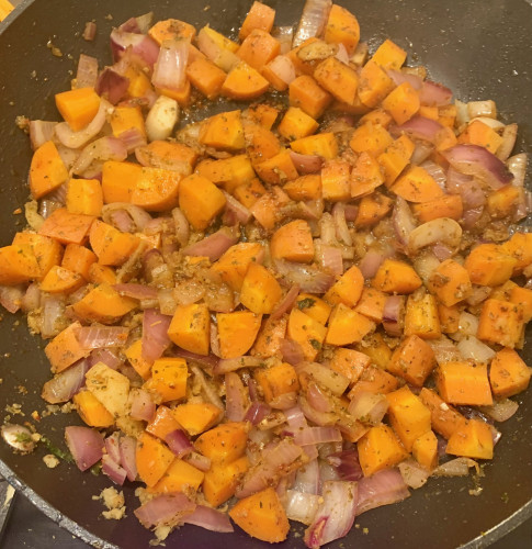 A skillet with chopped carrots andd red onion cooking.