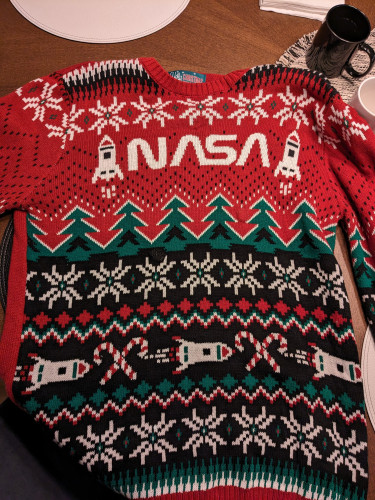 An ugly red and green Christmas sweater with the NASA worm logo at the top flanked on either side by rockets