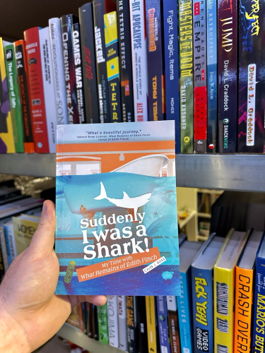A book called Suddenly I Was A Shark! held up against shelves full of video game books. 