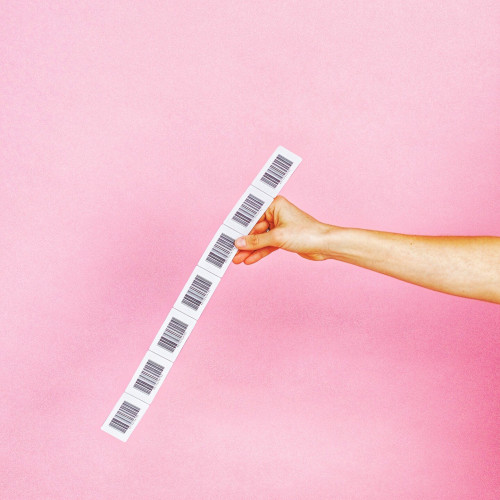 A person's arm and hand holding up a strip of bar codes in front of a bright pink background 