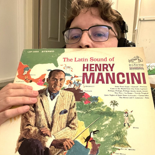 Vinyl lister hiding behind the cover to “The Latin Sounds of Henry Mancini” which has a cover featuring a drawing of Mancini in a suite in front of a map of South America.