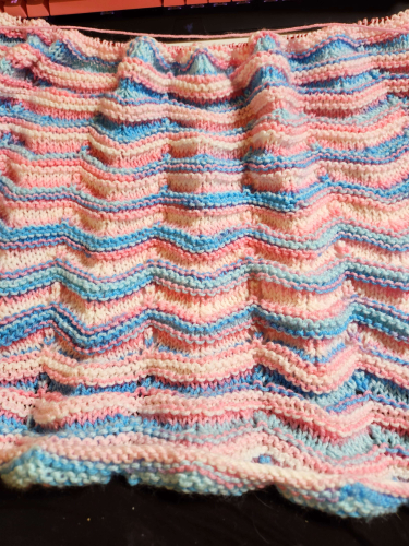 A knitted blanket, it has a wavy ridge pattern in pride flag colors. It is still a WIP.
