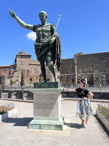 Dr G standing next to the 1930s era bronze of Augustus in Rome. The day is sunny and Dr G is smiling up at Augustus.