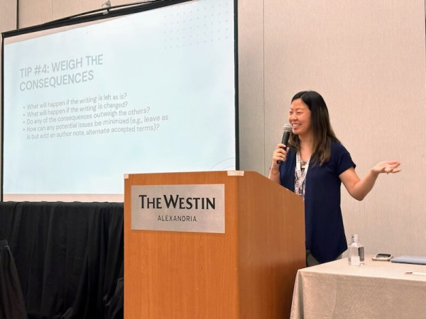 A Chinese American woman wearing a dark blue blouse standing behind a podium labeled "The Westin Alexandria" next to a projector screen