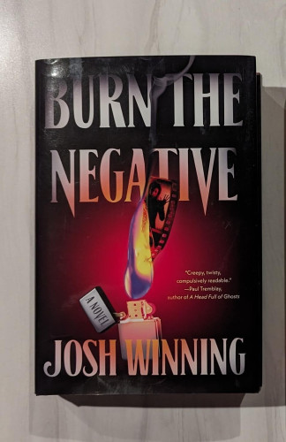 Hardcover of BURN THE NEGATIVE by Josh Winning. The title is written in white font at the top with the author's name at the bottom. In the center is a lighter, lit with a flame that is burning a strip of film.
