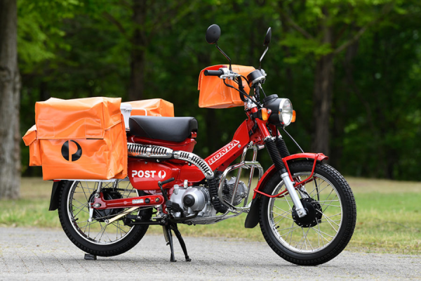 A red Honda step through motor cycle with orange water proof rubberised fabric paniers. Two large ones each side of the bike tail, and a moderate sized one on the back of the handle bars. 

All emblazoned with AusPost logos.