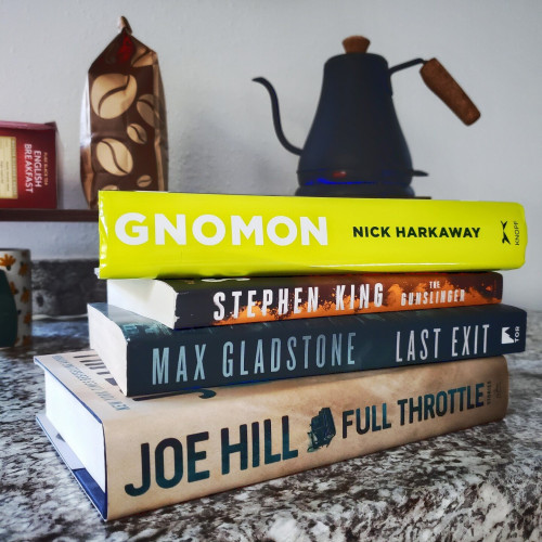 Stack of four books on a counter top. From top to bottom the books are Gnomon by Nick Harkaway, Gunslinger by Stephen King, The Last Exit by Max Gladstone, and Full Throttle by Joe Hill