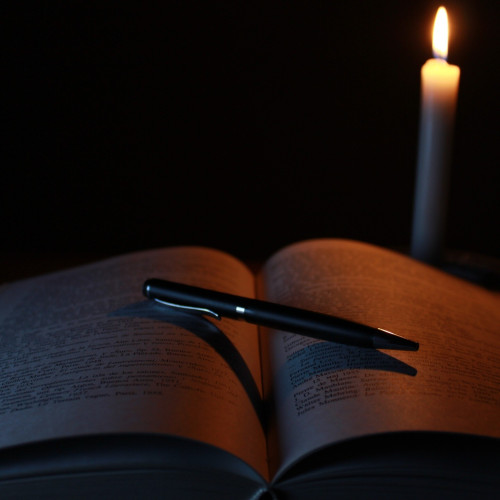 a pen on top of an open book in a dark room with a lit candle in teh background