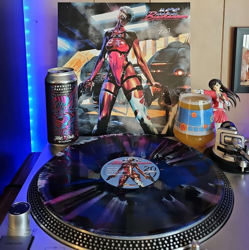 A Cyber Splatter vinyl record sits on a turntable. Behind the turntable, a vinyl album outer sleeve is displayed. The front cover shows a woman in a futuristic leotard outfit and face gear holding 2 guns in front of futuristic vehicles. 