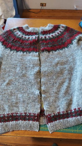 Stranded colorwork yoke sweater after steeking the opening. Main color is gray. Contrast colors are cranberry red and forest green.